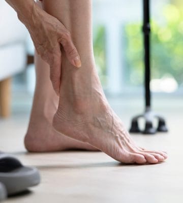 Senior woman holding ankle and suffering from foot arthritis pain.