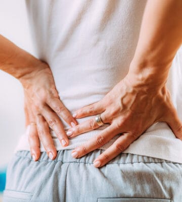Person with lower back pain holding their lower back with both hands
